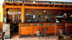 A bar area with wooden shelves displaying bottles, a stone counter, and bar stools. - Hotel Rural Las Farolas (El Espinar)