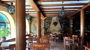 A restaurant with wooden tables and chairs, a stone wall, and hanging lanterns. - Hotel Rural Las Farolas (El Espinar)