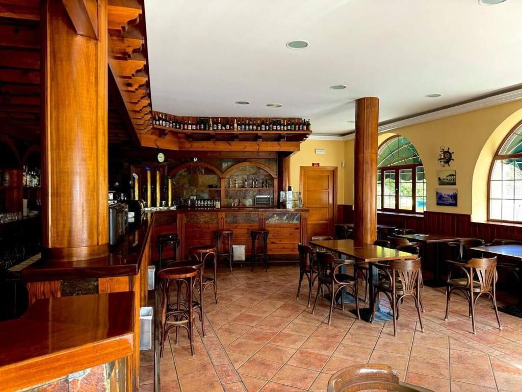 A restaurant with wooden bar and tables, a counter with bottles, and large windows.