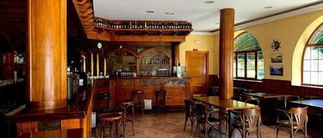 A restaurant with wooden bar and tables, a counter with bottles, and large windows.