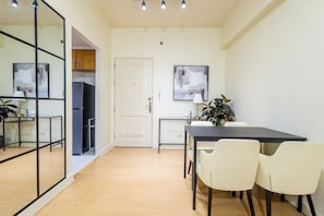 A modern kitchen with a refrigerator, a dining table with chairs, and a door leading to another room.