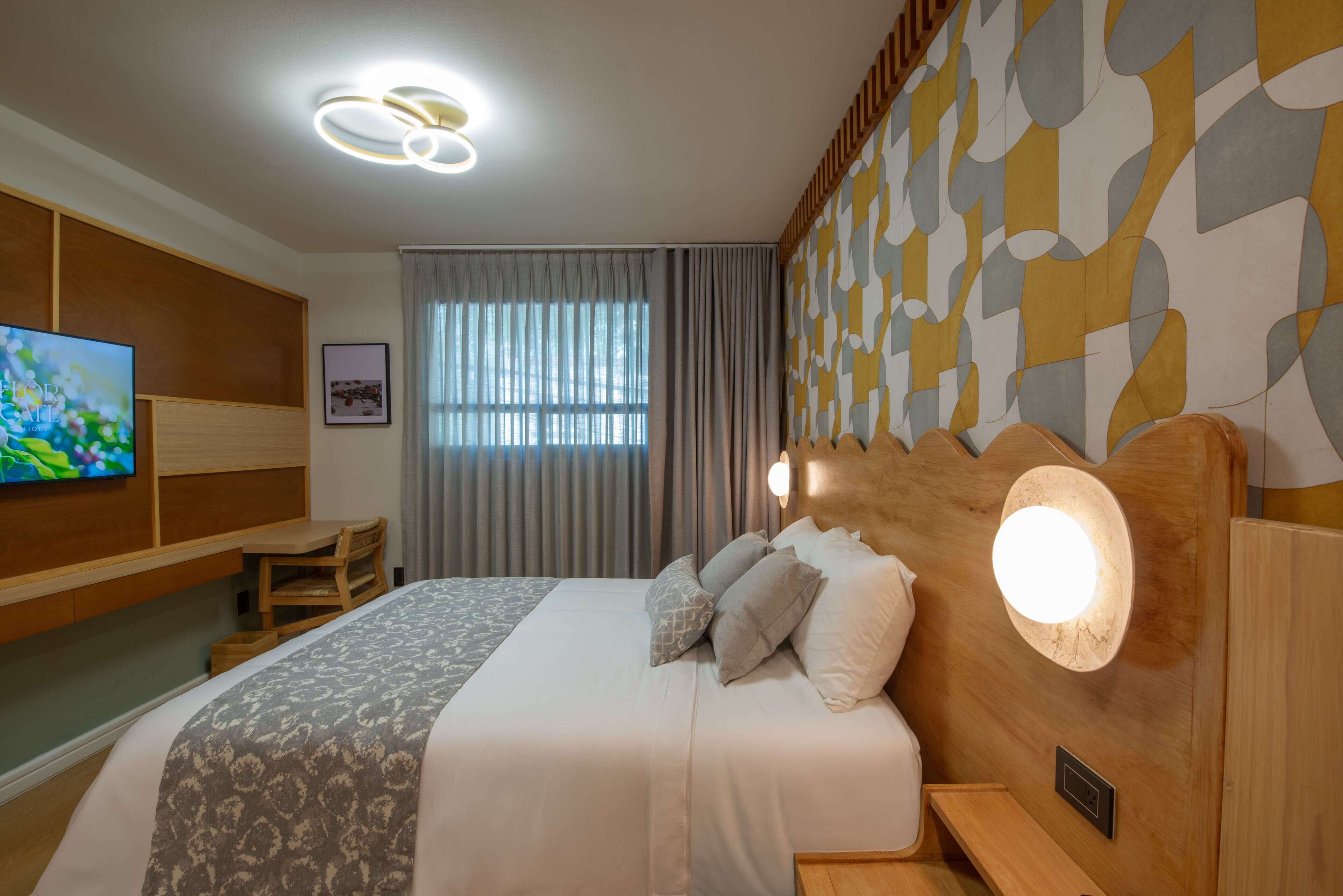 A hotel room with a large bed, a TV, a desk, and a patterned wall.