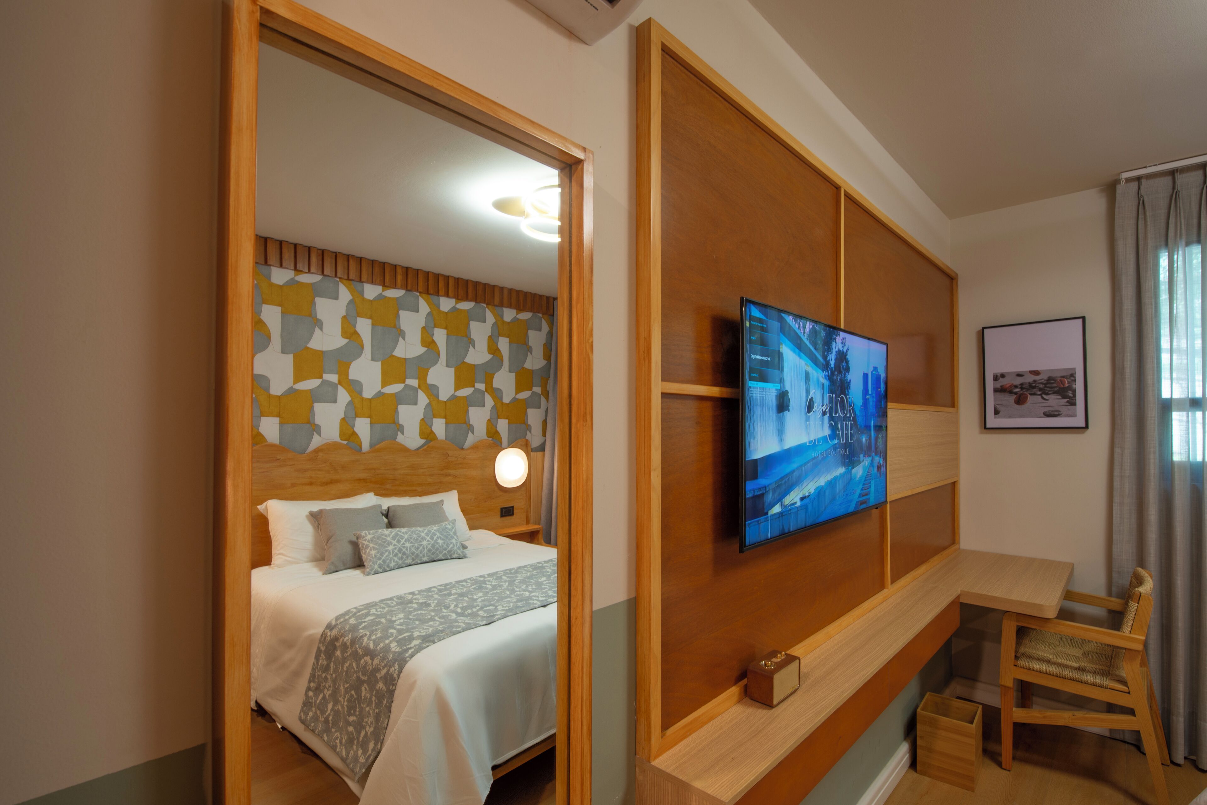 Una habitación de hotel con una cama, un televisor montado en la pared, un escritorio de madera y una silla.