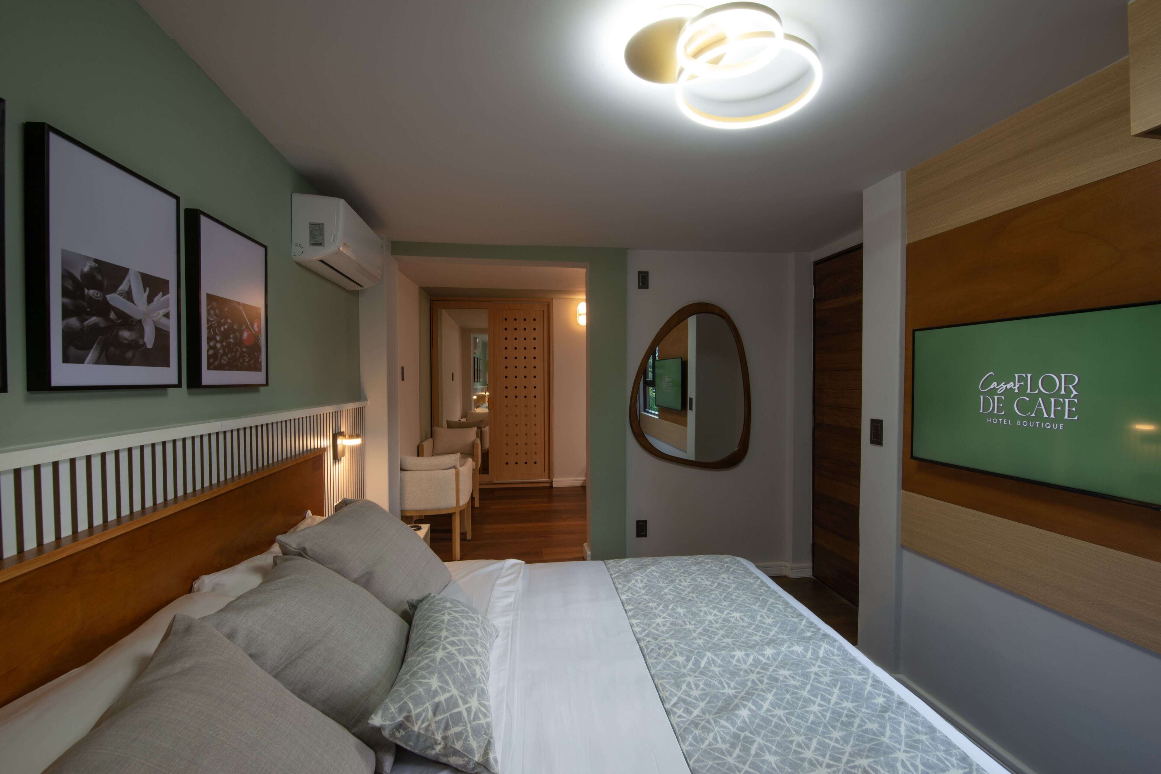 A hotel room with a bed, a TV, a mirror, and framed pictures on the wall.