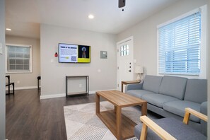 Ein modernes Wohnzimmer mit grauem Sofa, Couchtisch aus Holz und einem Fernseher, der 'TOWER OF THE AMERICAS' zeigt.