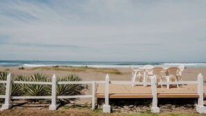Een strand met een houten terras, witte stoelen, een witte omheining en uitzicht op de oceaan.