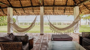Een overdekt terras met rieten meubels, een hangmat en uitzicht op de oceaan.
