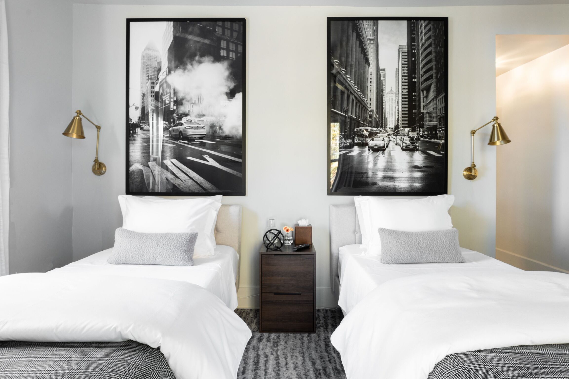A hotel room with two beds, a nightstand, and two wall-mounted lamps.
