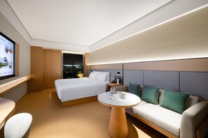 Une chambre d’hôtel moderne dotée d’un grand lit, d’un canapé, d’une table ronde et d’un écran de télévision diffusant une vue panoramique sur la ville.