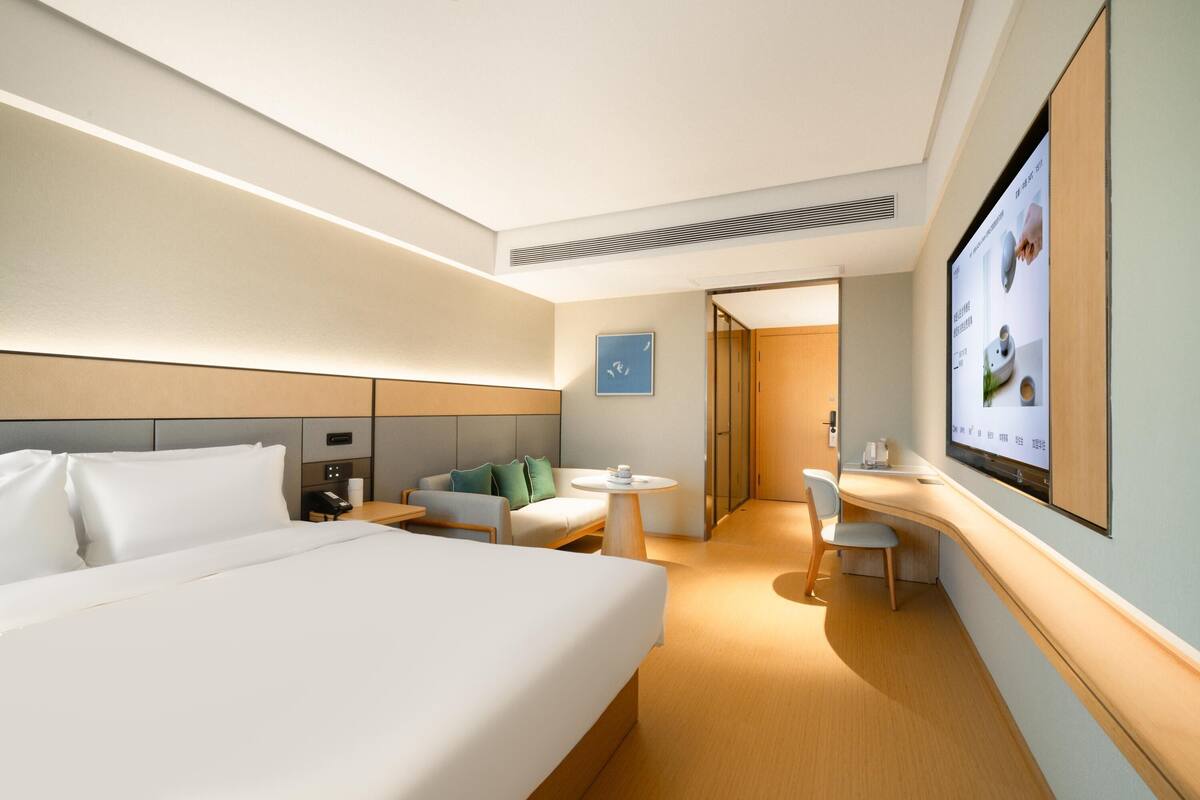 Ein modernes Hotelzimmer mit einem großen Bett, einer Couch, einem kleinen Tisch und einem an der Wand montierten Fernseher.