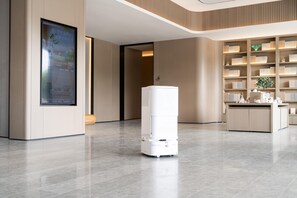 A modern hotel lobby with a large digital screen, a central white pillar, and a reception desk with a bookshelf.