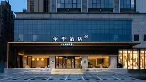 A modern hotel entrance with a large glass facade, a sign reading "JI HOTEL", and a well-lit entrance area.