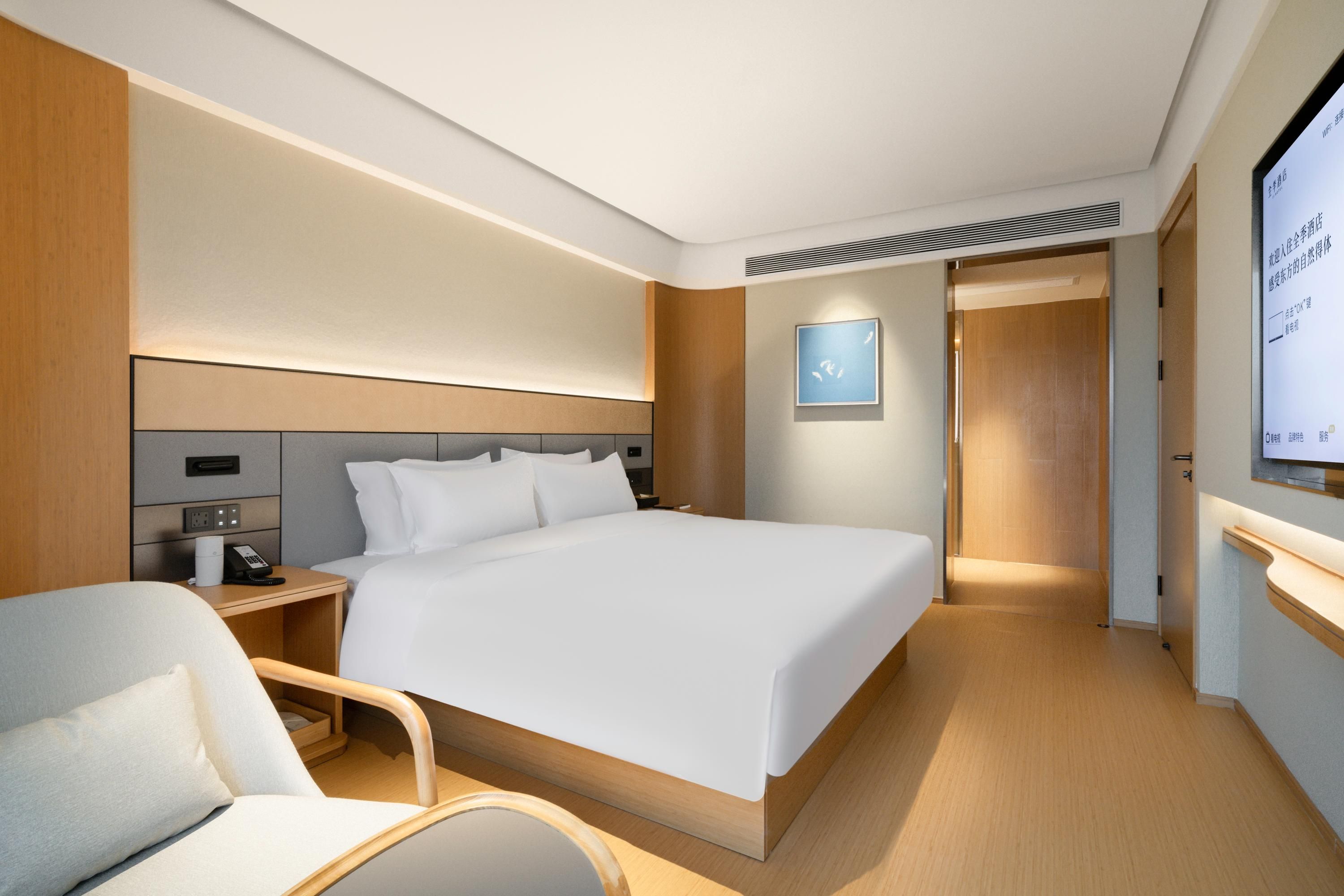 Una habitación de hotel moderna con una cama grande, mesita de noche, una silla y una pantalla de televisión.