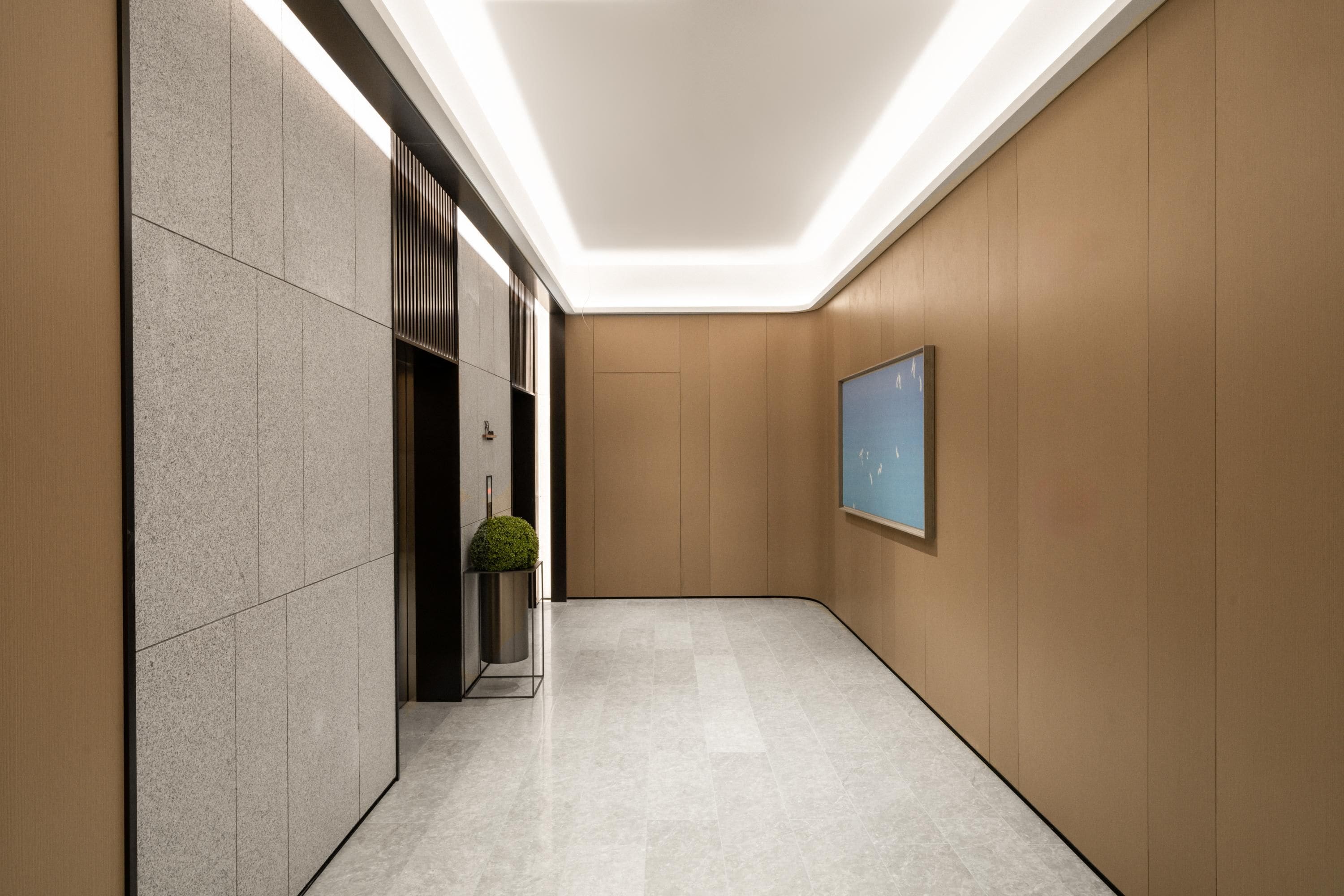 A modern hallway with a marble floor, a potted plant, and a framed picture on the wall.