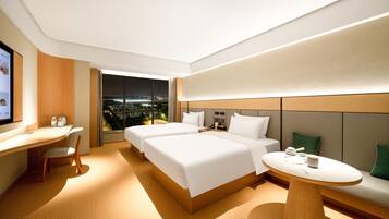A modern hotel room with two beds, a desk, and a view of the city at night.