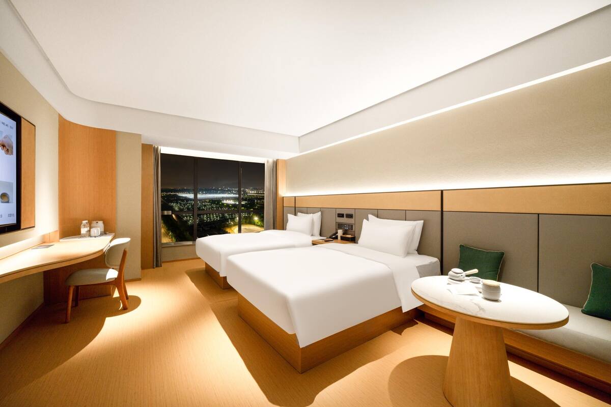 Ein modernes Hotelzimmer mit zwei Betten, einem Schreibtisch und Blick auf die beleuchtete Stadt.