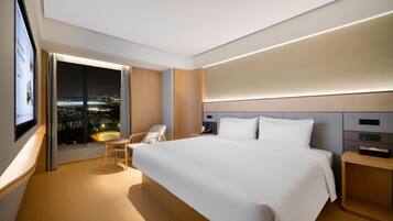 A modern hotel room with a large bed, a desk, a chair, and a TV screen displaying a cityscape view.