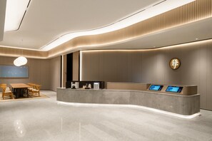 Ein moderner Hotel-Empfangsbereich mit einer gebogenen Rezeption, einer Sitzecke mit Tisch und Stühlen sowie einem großen, an der Wand befestigten Bildschirm.