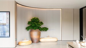 A modern reception area with a large vase of greenery, a digital display, and a reception desk with amenities.