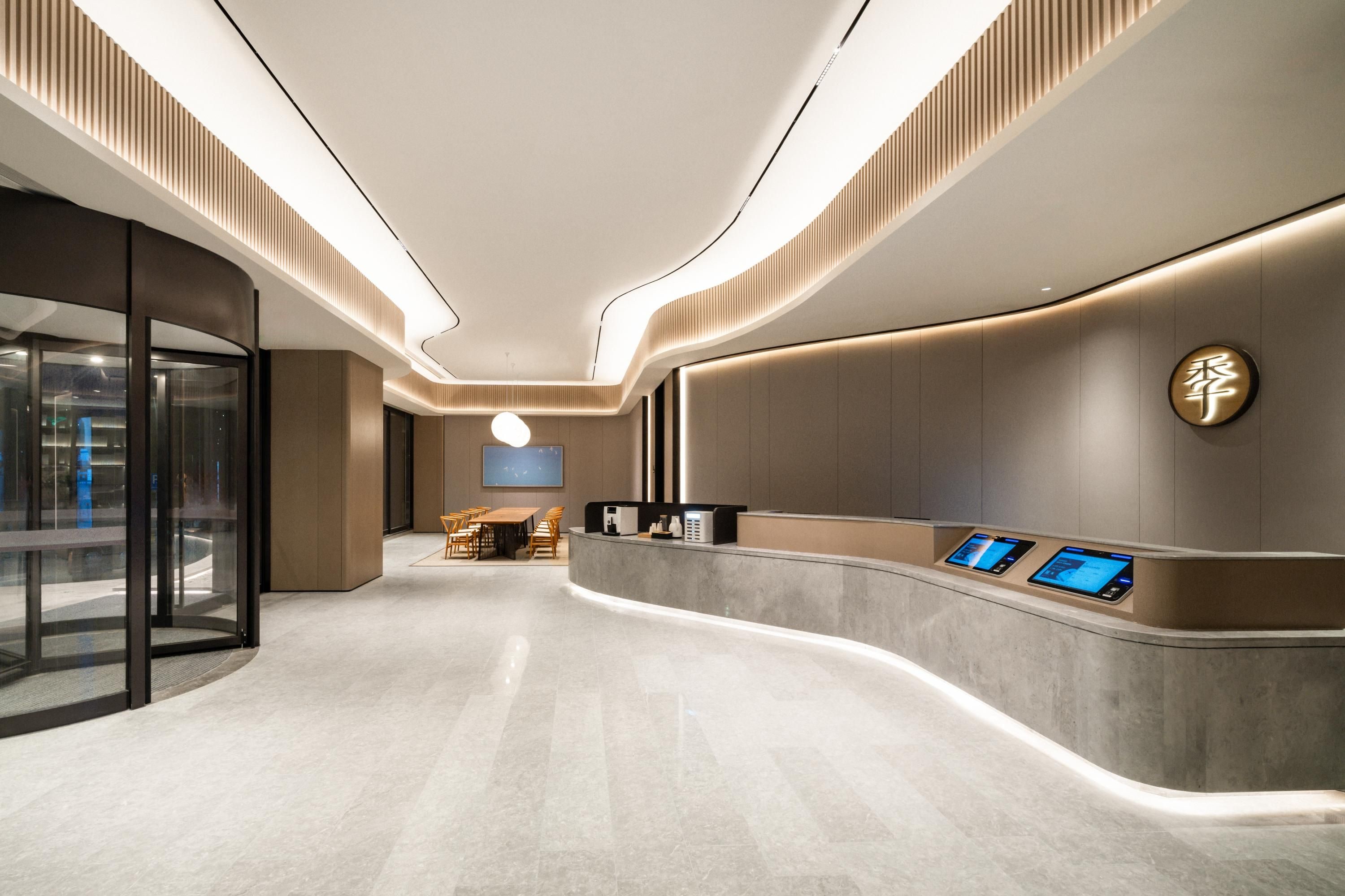 Un moderno vestíbulo de hotel con un mostrador de recepción curvo, puertas de cristal y una zona de estar.