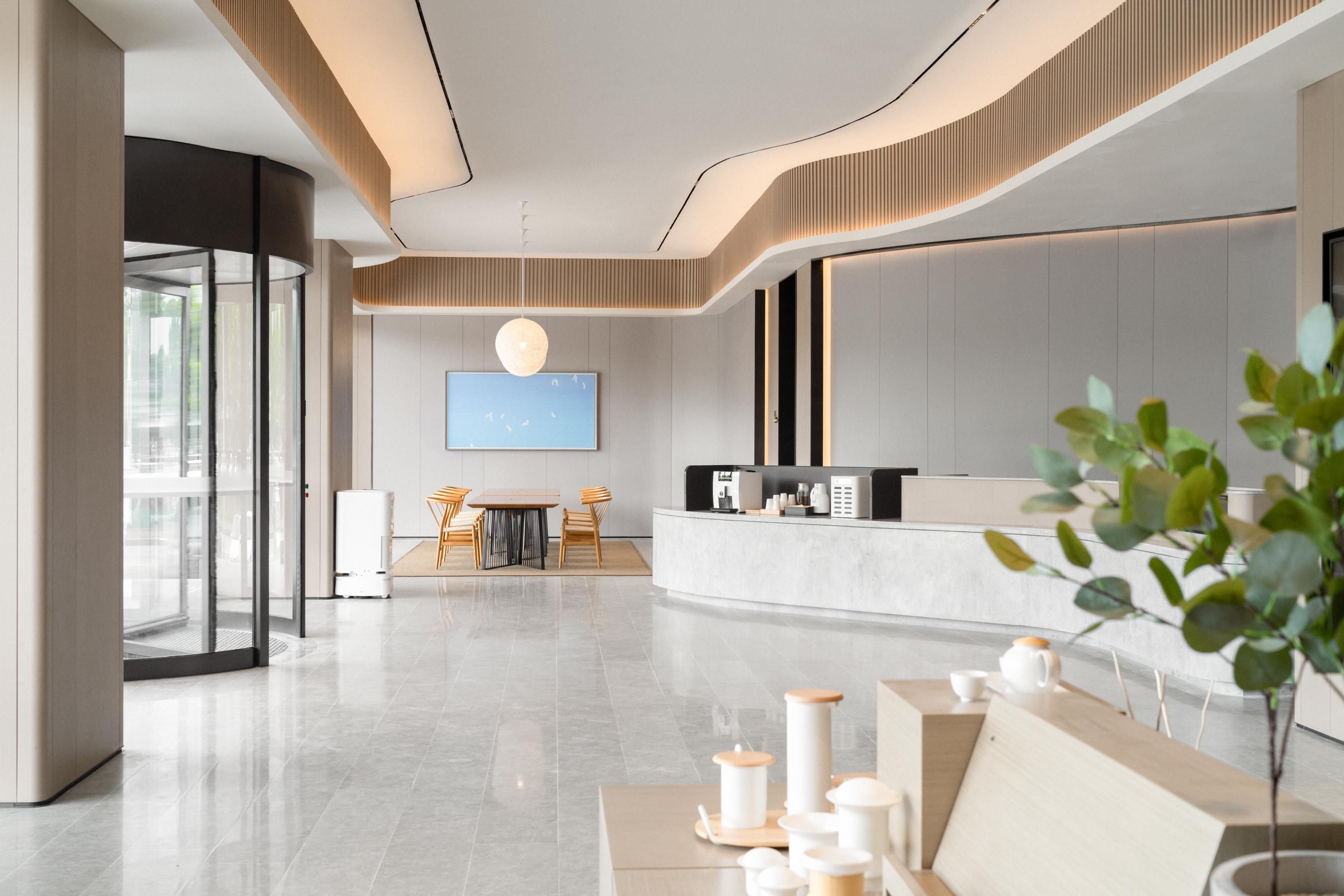 A modern hotel lobby with a reception desk, seating area, and a large flat-screen TV.