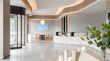 A modern hotel lobby with a reception desk, seating area, and a large flat-screen TV.