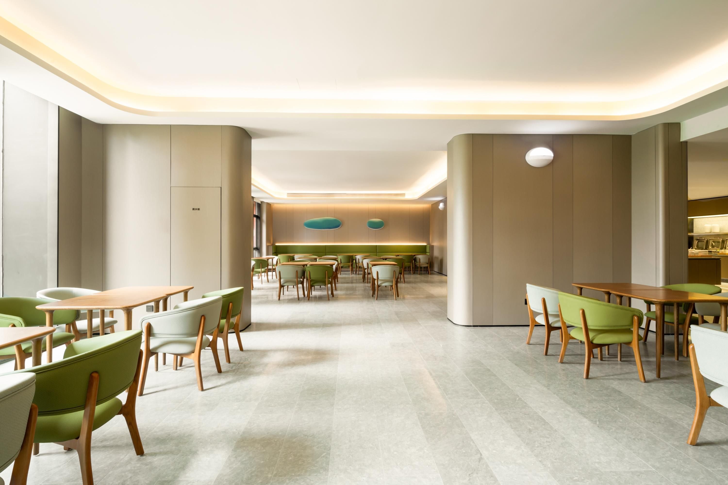 A modern dining area with green and white chairs, wooden tables, and a central seating area with a long table.