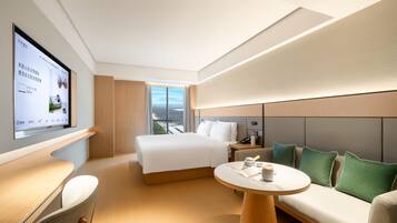 Una habitación de hotel moderna con una cama grande, un sofá, una mesita y un televisor montado en la pared.