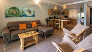 Una sala de estar moderna con un sofá, una mesa de centro y un comedor con sillas, y una cocina al fondo.