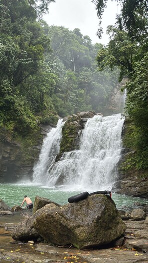 A waterfall in a forested area with rocks and a person near the water. - Condominio mirasol - luna  (Bahía Ballena)
