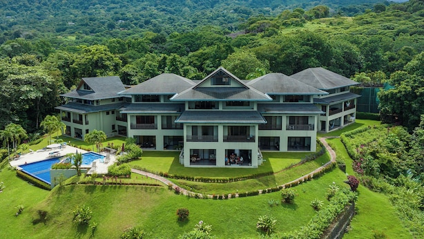 Un hotel grande de varios pisos con piscina, rodeado de exuberante vegetación y colinas.