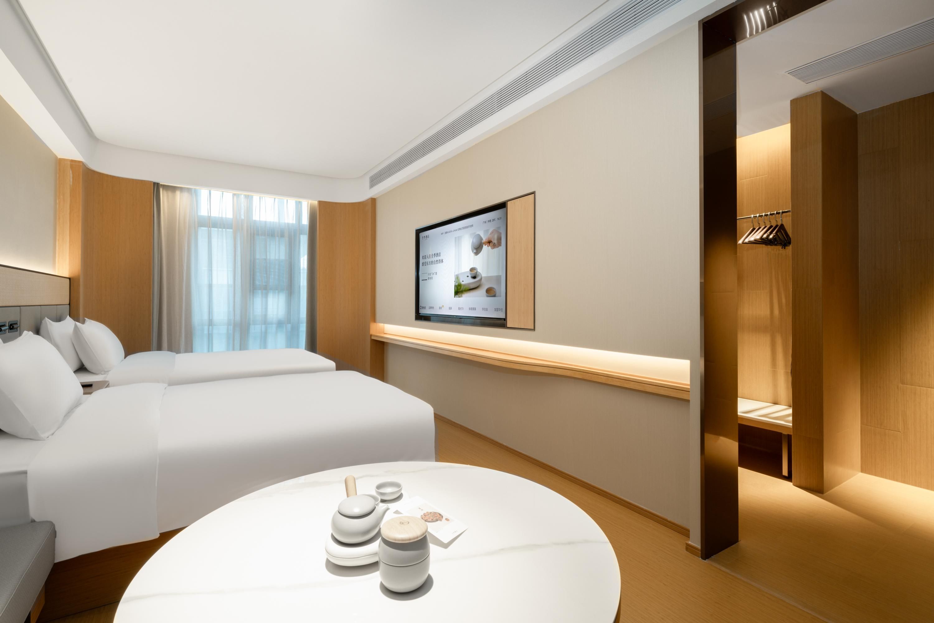 Una habitación de hotel moderna con una cama grande, una mesa redonda con juegos de té, un televisor montado en la pared y un revestimiento de pared de madera.