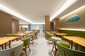 A modern dining area with green and white chairs, wooden tables, and a central light fixture.