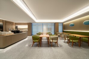 Ein modernes Esszimmer mit einem zentralen Tisch, umgeben von Stühlen, einer Theke mit Speisen und einer Sitzecke mit einem grünen Sofa.