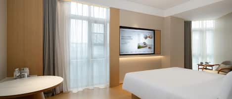 A hotel room with a bed, a desk, a TV mounted on the wall, and a window with curtains.
