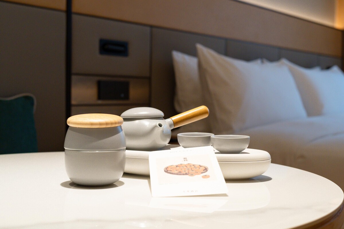 Ein ordentlich aufgestelltes Teeservice auf einem Tisch, im Hintergrund ein Bett.