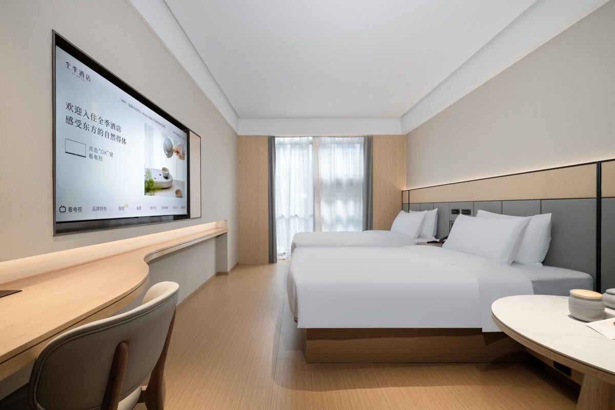 Ein Hotelzimmer mit Bett, Schreibtisch, Stuhl, Fernseher und einem Fenster mit Vorhängen.