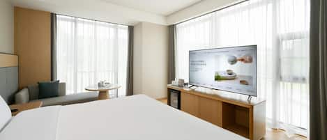 A hotel room with a large bed, a TV on a wooden stand, a small table with a cup and saucer, and a sofa.
