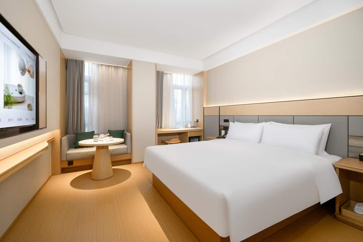 A modern hotel room with a large bed, a desk, a chair, and a TV mounted on the wall.