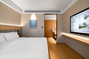 A modern hotel room with a large bed, a TV mounted on the wall, and a wooden nightstand.