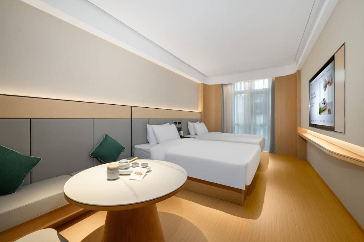A modern hotel room with a large bed, a round table with a lamp, and a TV mounted on the wall.