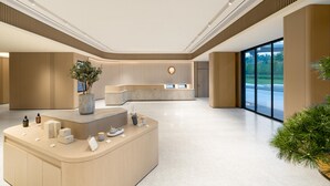 A modern reception area with a curved desk, potted plants, and a large window offering a view of the outdoors. - Ji Hotel Guangzhou Tianhe Smart City Wetland Park (Guangzhou)