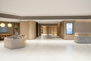 Eine moderne Hotelhalle mit Rezeption, Sitzbereich und einem großen Bildschirm, der Informationen anzeigt.