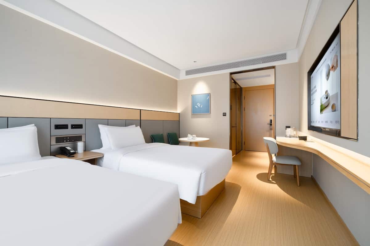 A hotel room with two beds, a desk, a chair, a small table, and a television.