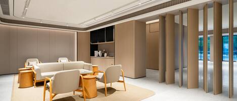 A modern, well-lit lounge area with a sofa set, wooden side tables, and a large window offering a view.