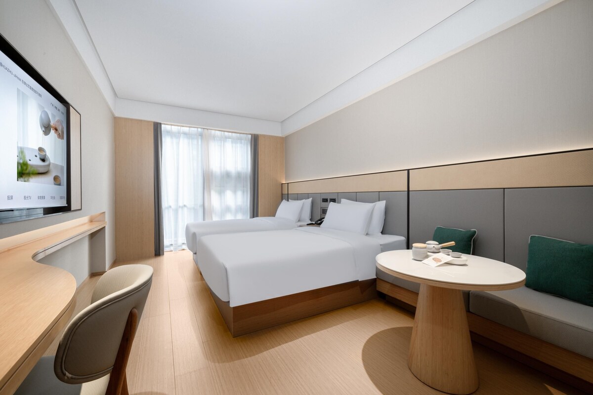 Una habitación de hotel moderna con una cama grande, un escritorio, una mesa redonda y un televisor en la pared.