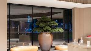 A modern reception area with a large potted plant, wooden seating, and a glass wall reflecting the cityscape. - Ji Hotel Guangzhou Tianhe Smart City Wetland Park (Guangzhou)