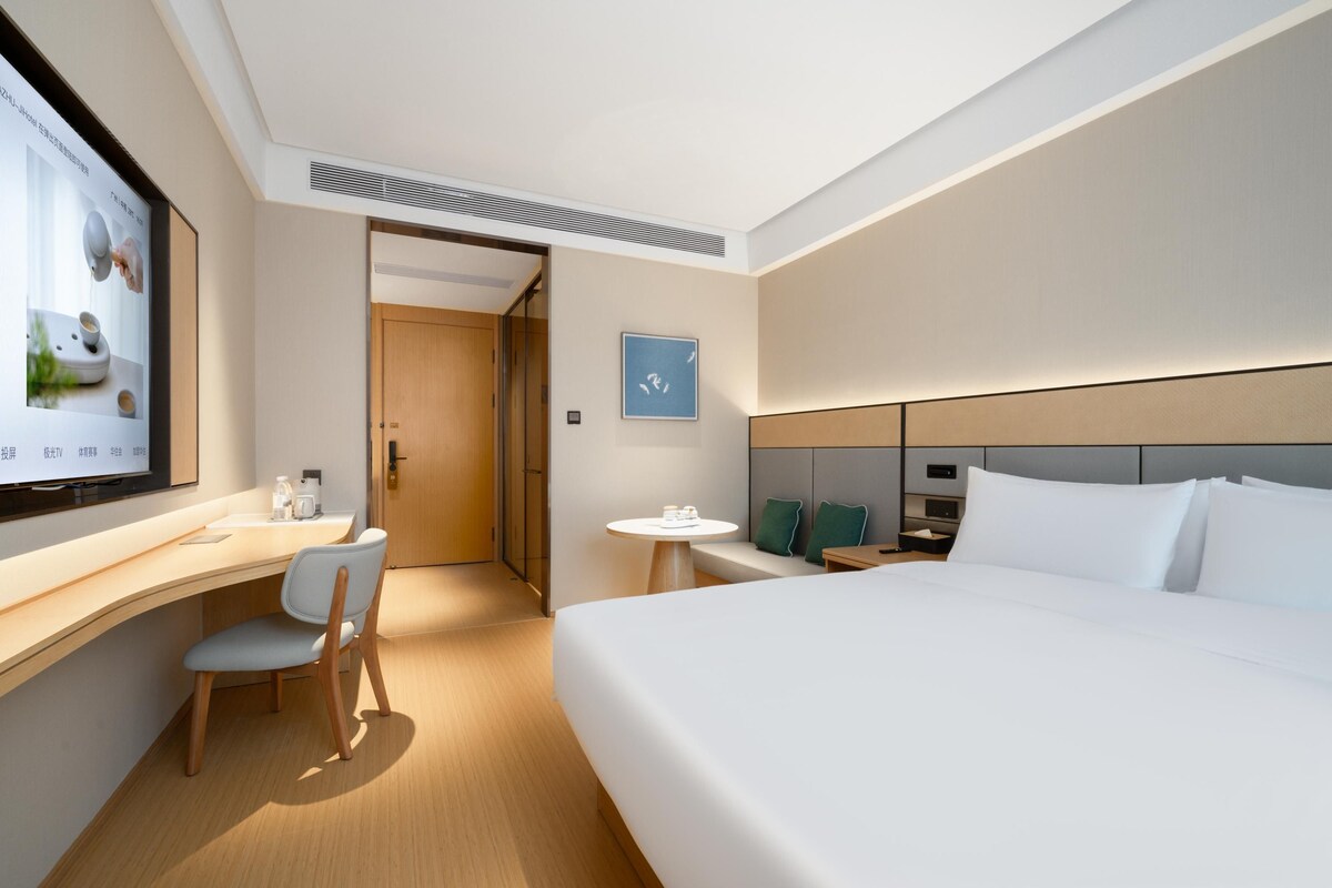 Una habitación de hotel moderna con una cama grande, un escritorio con silla, una mesita redonda y un televisor montado en la pared.