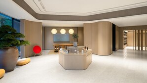 A modern lobby with a central reception desk, a large potted plant, and a seating area with chairs. - Ji Hotel Guangzhou Tianhe Smart City Wetland Park (Guangzhou)