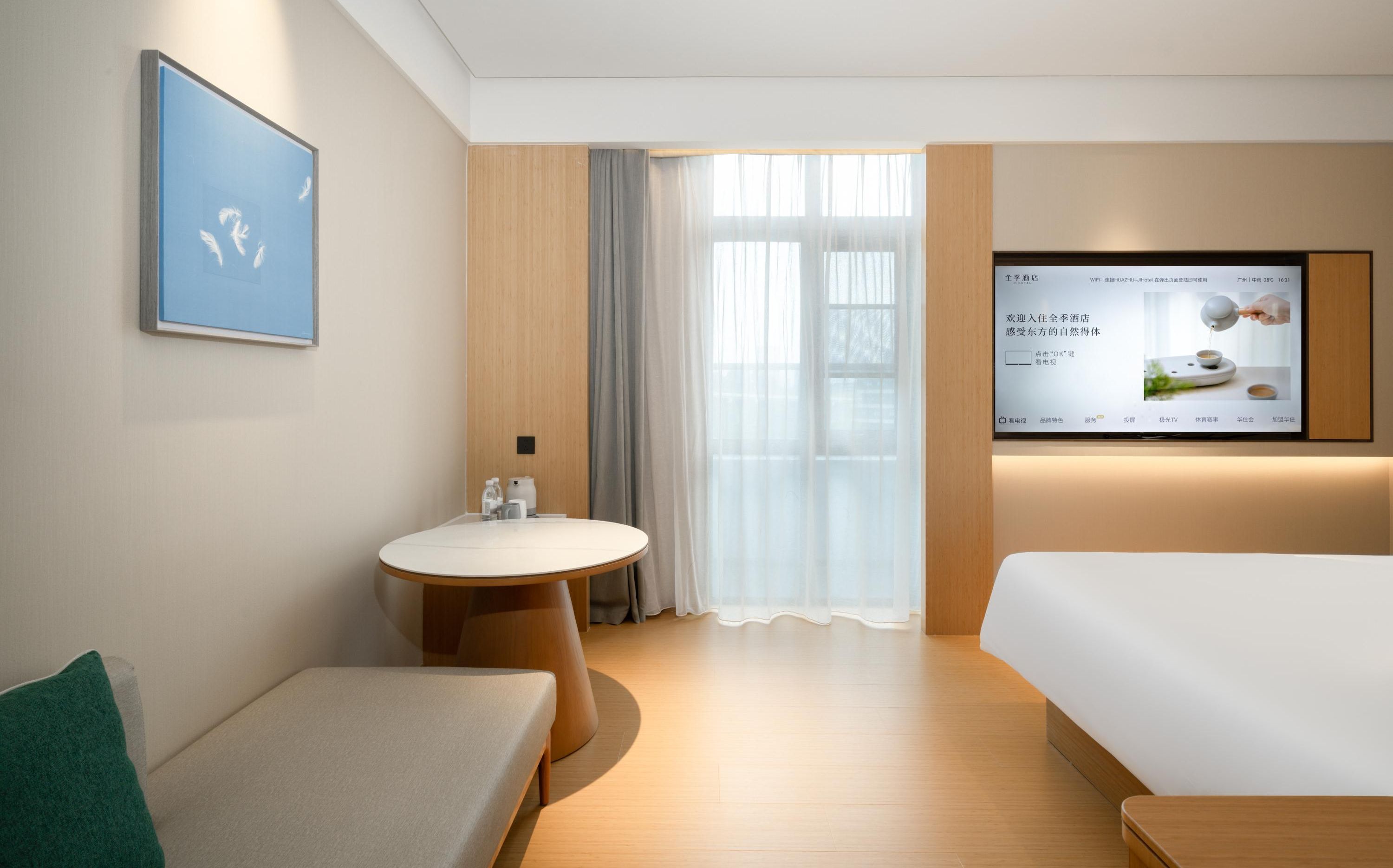 Ein Hotelzimmer mit Bett, rundem Tisch mit Stuhl, kleinem Waschbecken und Fernseher, der eine Speisekarte zeigt.